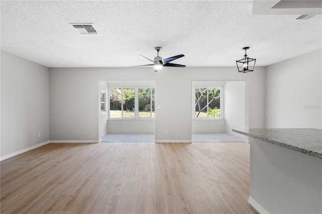 unfurnished living room with light wood-style flooring, a textured ceiling, visible vents, and baseboards