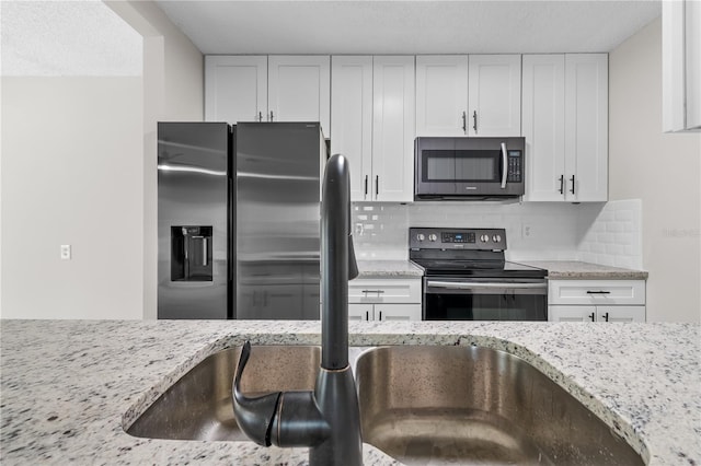 kitchen with stainless steel appliances, decorative backsplash, light stone countertops, and white cabinets