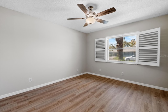 empty room with a textured ceiling, light wood finished floors, a ceiling fan, and baseboards