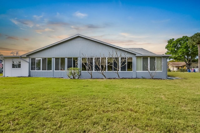 back of house at dusk featuring a sunroom and a lawn