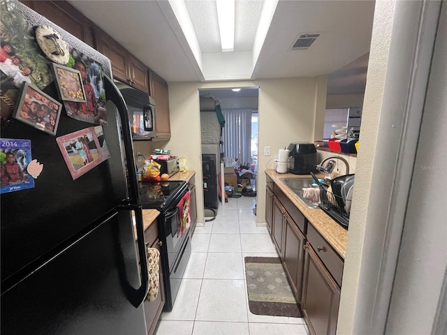 kitchen featuring light tile patterned floors, light countertops, visible vents, a sink, and black appliances