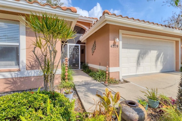 doorway to property featuring a tile roof, stucco siding, an attached garage, a gate, and driveway