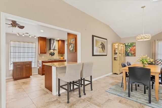 kitchen with decorative backsplash, brown cabinetry, vaulted ceiling, wall chimney range hood, and gas stovetop