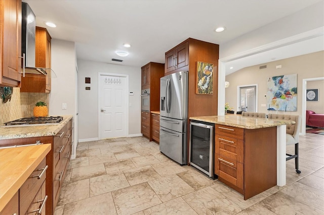 kitchen featuring wine cooler, stainless steel appliances, visible vents, backsplash, and a kitchen bar