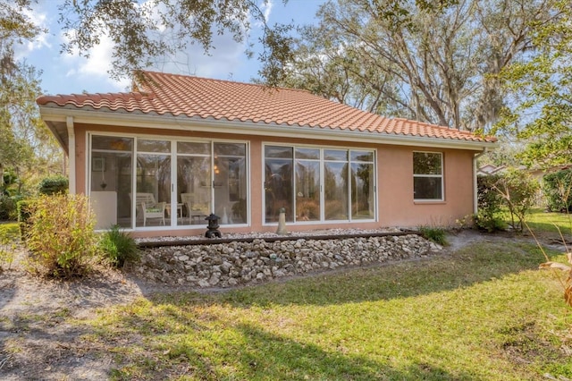 back of property featuring stucco siding, a lawn, and a tiled roof