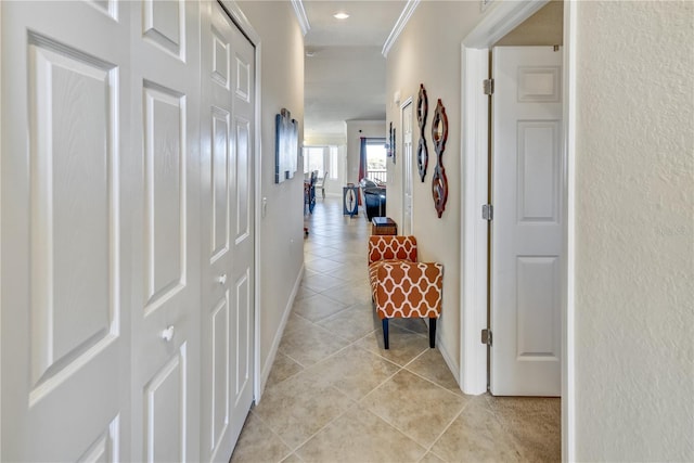 hallway with a textured wall, crown molding, baseboards, and light tile patterned floors