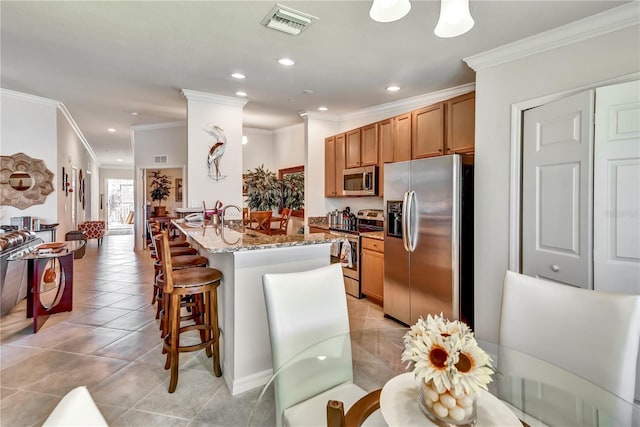 kitchen featuring light tile patterned floors, visible vents, brown cabinetry, appliances with stainless steel finishes, and light stone countertops