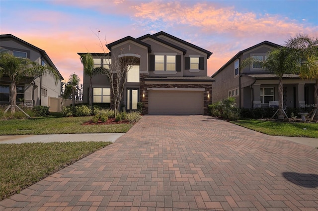 view of front facade with a garage, decorative driveway, stone siding, and stucco siding