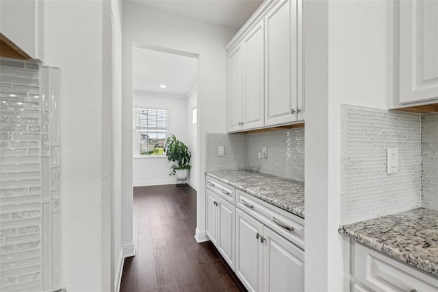 kitchen with light stone counters, baseboards, white cabinets, backsplash, and dark wood-style floors