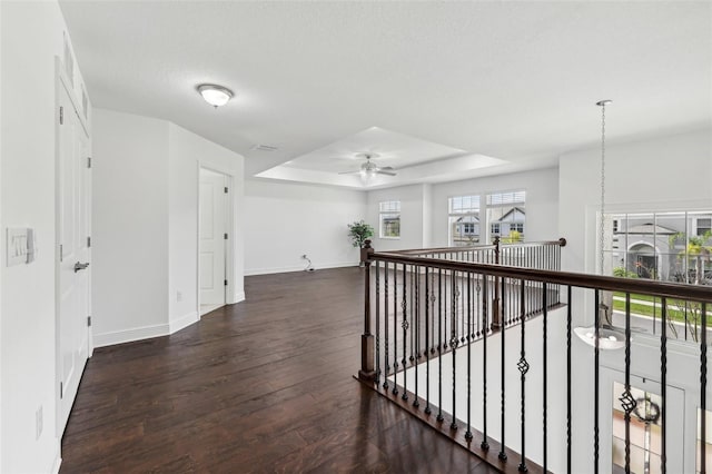 corridor with an upstairs landing, a raised ceiling, baseboards, and wood finished floors