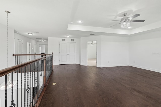 empty room featuring a tray ceiling, dark wood-style flooring, visible vents, ceiling fan, and baseboards