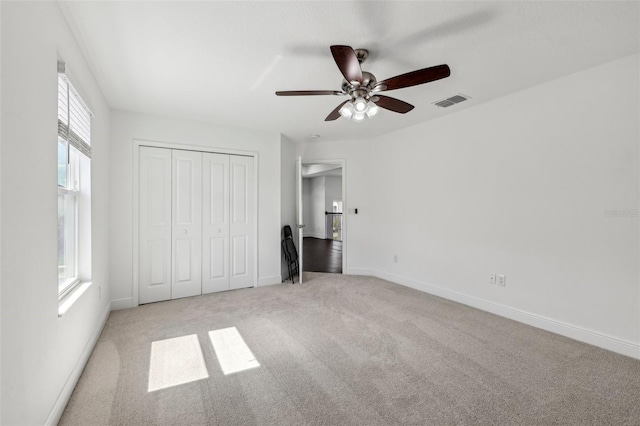 unfurnished bedroom with baseboards, visible vents, light colored carpet, ceiling fan, and a closet