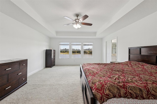 bedroom with ceiling fan, light carpet, baseboards, a tray ceiling, and ensuite bath