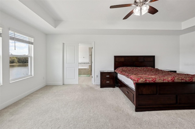 bedroom featuring connected bathroom, light colored carpet, a ceiling fan, baseboards, and a tray ceiling