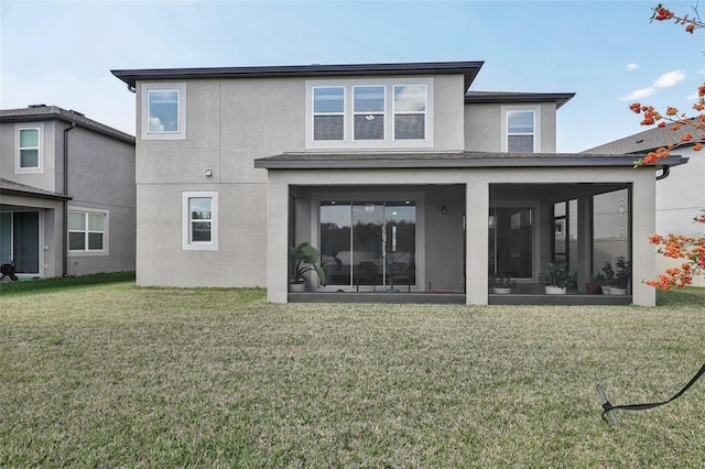 back of property featuring a sunroom, a lawn, and stucco siding