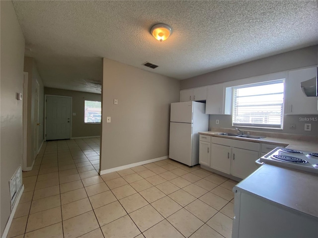 kitchen with a sink, plenty of natural light, white cabinetry, freestanding refrigerator, and light tile patterned floors