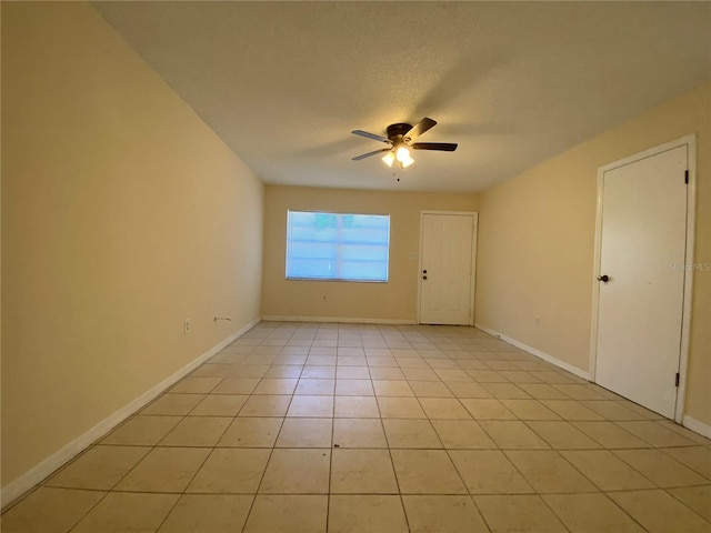 empty room with light tile patterned flooring, a ceiling fan, baseboards, and a textured ceiling