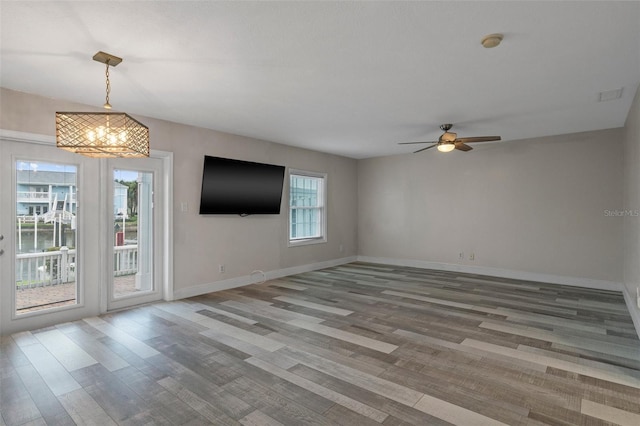 unfurnished living room featuring visible vents, ceiling fan with notable chandelier, a wealth of natural light, and baseboards