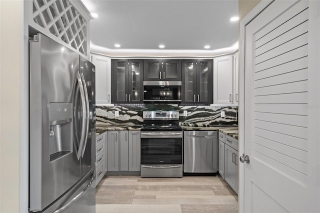 kitchen featuring stainless steel appliances, recessed lighting, decorative backsplash, light wood-style floors, and glass insert cabinets