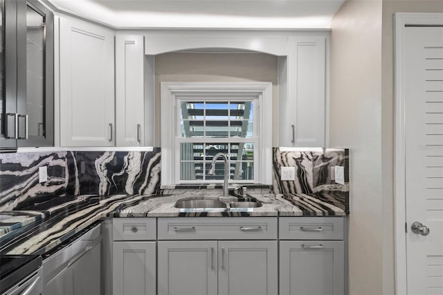 kitchen featuring light stone counters, backsplash, glass insert cabinets, white cabinets, and a sink