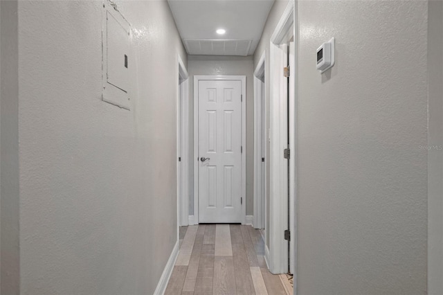 hall featuring light wood-style floors, a textured wall, and baseboards