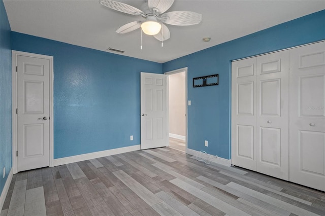 unfurnished bedroom featuring a closet, visible vents, a ceiling fan, wood finished floors, and baseboards