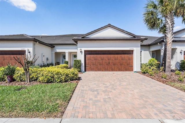 view of front of home with decorative driveway, an attached garage, and stucco siding