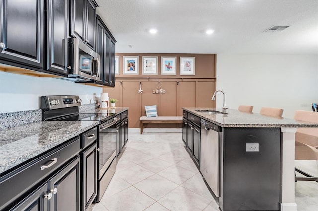 kitchen with visible vents, a kitchen breakfast bar, dark cabinets, stainless steel appliances, and a sink