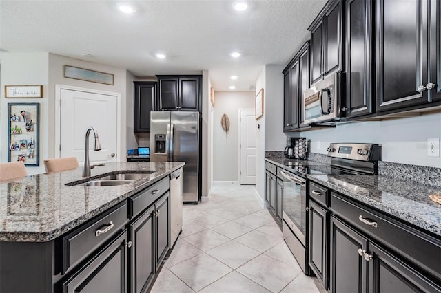 kitchen featuring stainless steel appliances, stone countertops, a sink, and dark cabinets