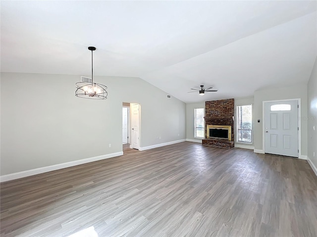 unfurnished living room featuring baseboards, wood finished floors, vaulted ceiling, a fireplace, and ceiling fan with notable chandelier