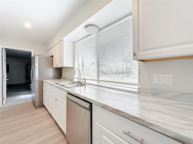 kitchen with stainless steel appliances, a sink, light stone countertops, and white cabinets