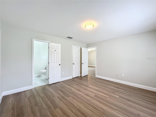 unfurnished bedroom featuring visible vents, baseboards, wood finished floors, and ensuite bathroom