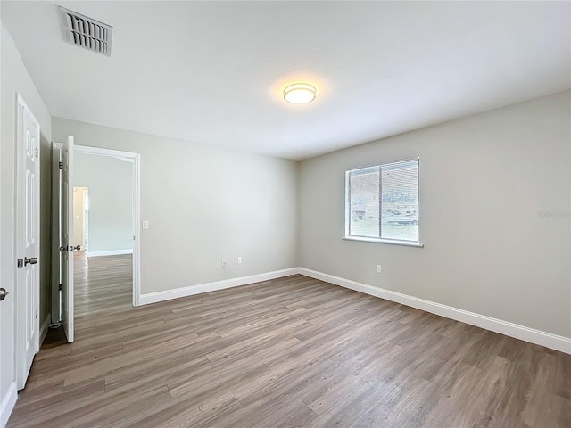 spare room featuring light wood finished floors, visible vents, and baseboards