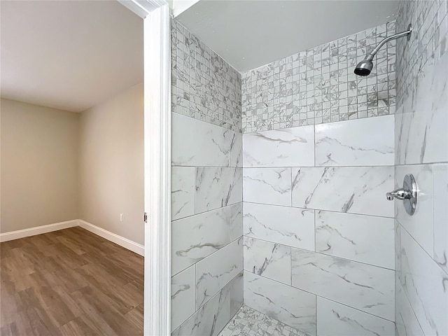 full bathroom featuring a tile shower, baseboards, and wood finished floors