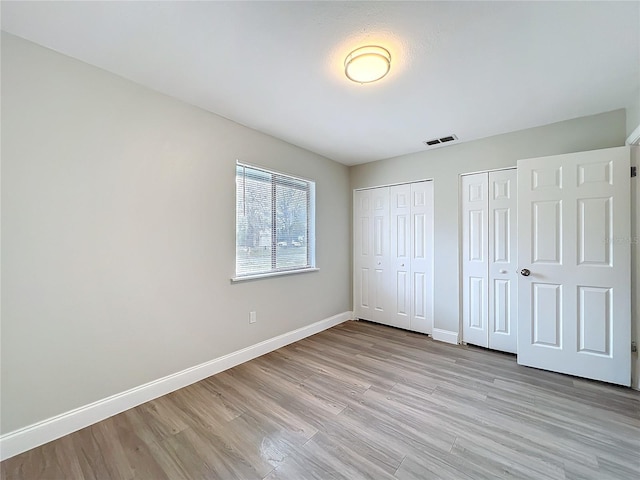 unfurnished bedroom with light wood-type flooring, visible vents, baseboards, and two closets