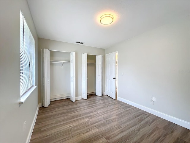 unfurnished bedroom featuring visible vents, baseboards, multiple closets, and wood finished floors