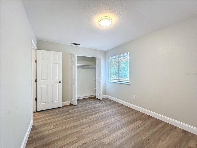 unfurnished bedroom featuring a closet, visible vents, light wood-style flooring, and baseboards