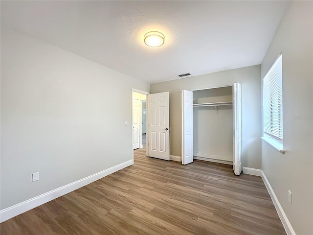 unfurnished bedroom featuring baseboards, a closet, visible vents, and wood finished floors