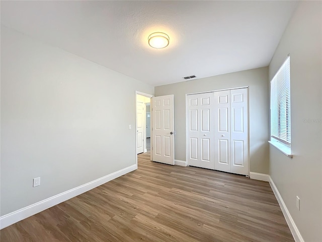 unfurnished bedroom featuring baseboards, a closet, visible vents, and wood finished floors