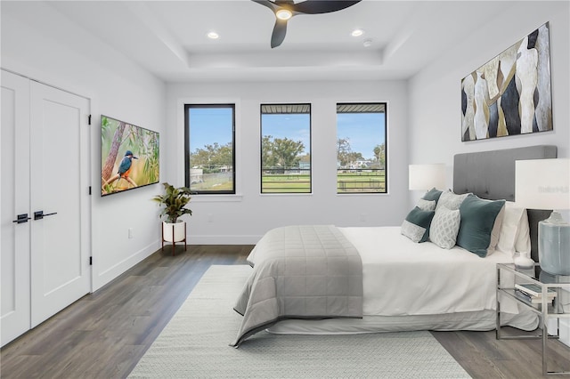 bedroom with recessed lighting, a raised ceiling, dark wood finished floors, and baseboards