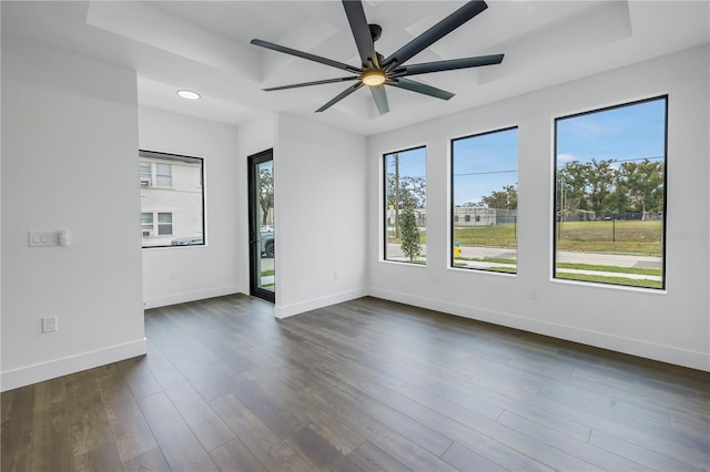 unfurnished room with a tray ceiling, dark wood-style flooring, a ceiling fan, and baseboards