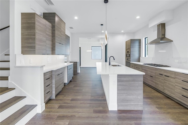 kitchen with a kitchen island with sink, light countertops, wall chimney range hood, and modern cabinets