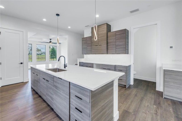 kitchen featuring an island with sink, pendant lighting, light countertops, and a sink