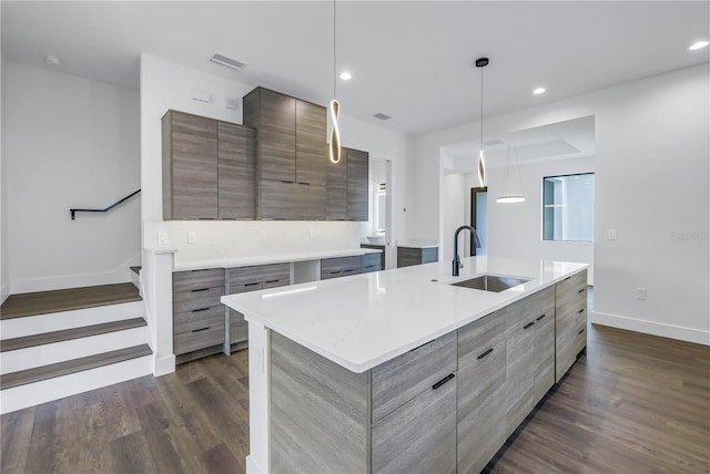 kitchen featuring a kitchen island with sink, a sink, light countertops, modern cabinets, and pendant lighting