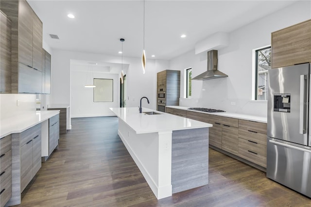 kitchen featuring a center island with sink, wall chimney exhaust hood, modern cabinets, appliances with stainless steel finishes, and light countertops