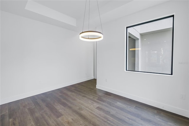 empty room with dark wood-type flooring, a raised ceiling, and baseboards