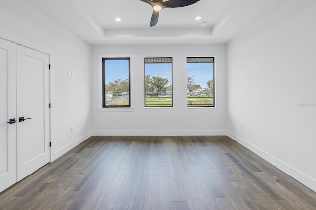 spare room featuring a raised ceiling, dark wood finished floors, and baseboards