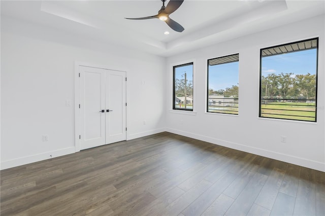 empty room with baseboards, a tray ceiling, dark wood-type flooring, and recessed lighting