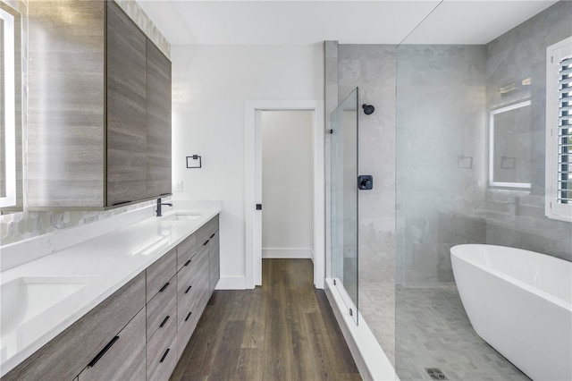 bathroom featuring double vanity, a soaking tub, a sink, a shower stall, and wood finished floors