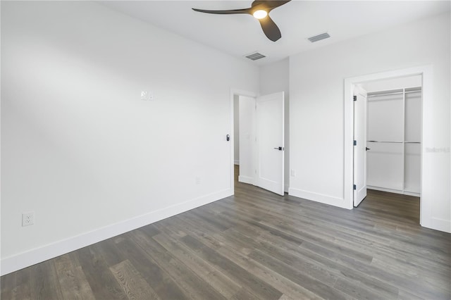 unfurnished bedroom with dark wood-style floors, a walk in closet, visible vents, and baseboards